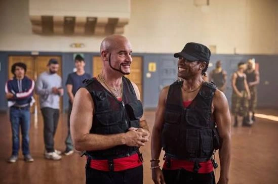 Two men wearing black vests over red exercise clothes exchange smiles