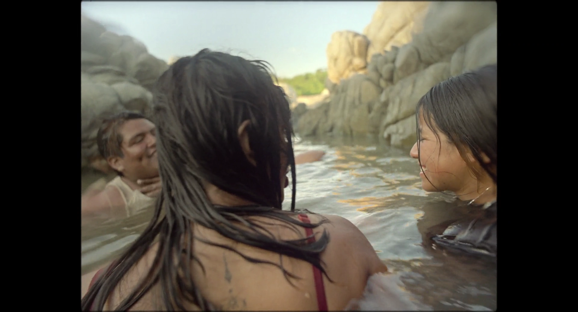 Several people in water between tall rocks, with a woman facing away in the foreground