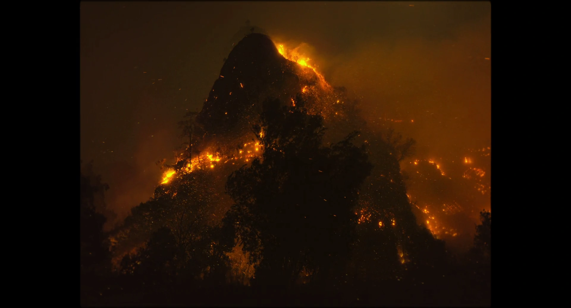 Mountain peaks at night with orange fires spreading through dense smoke