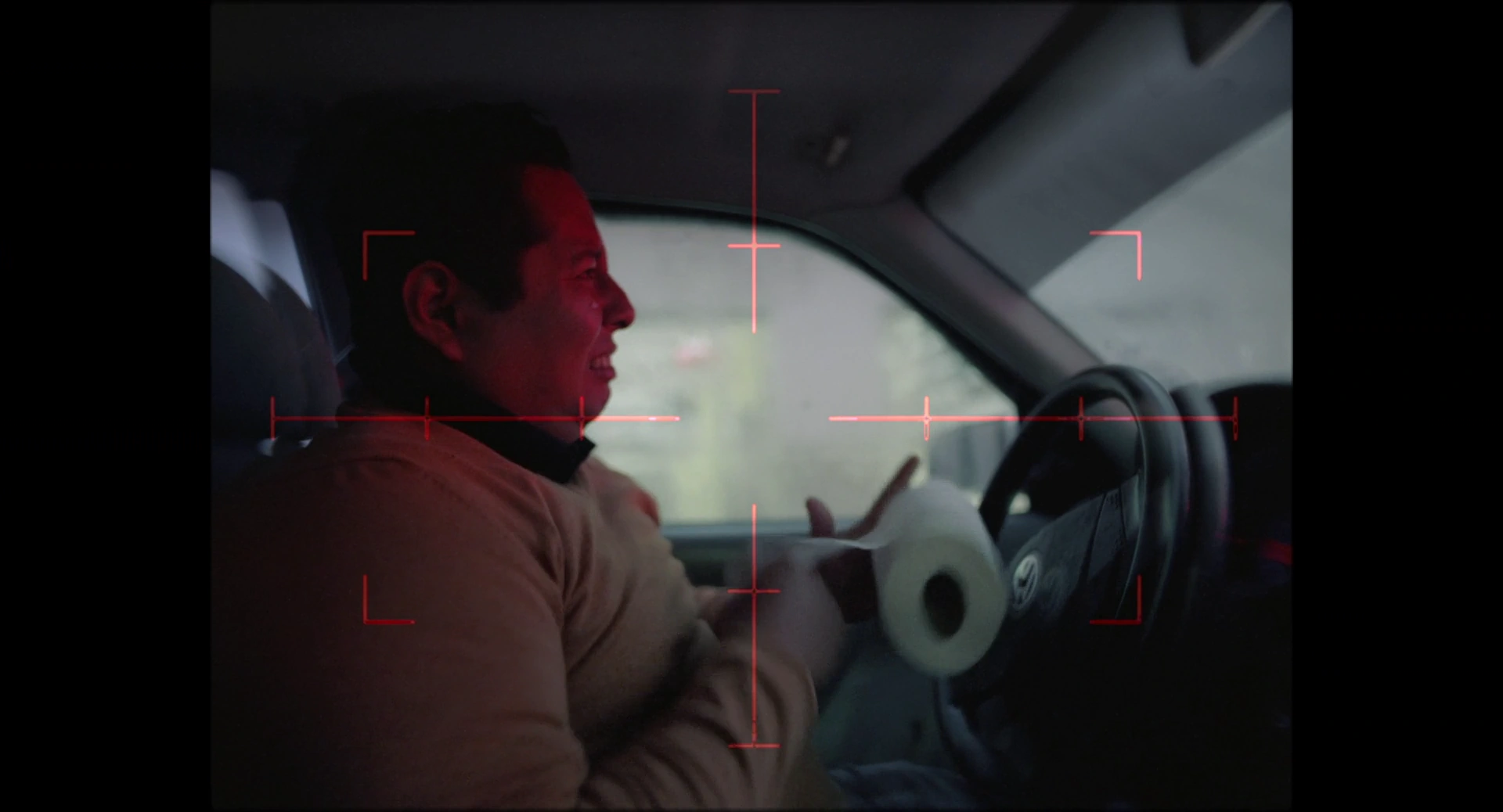 A man drives a car in an image containing red markers near the steering wheel and his face