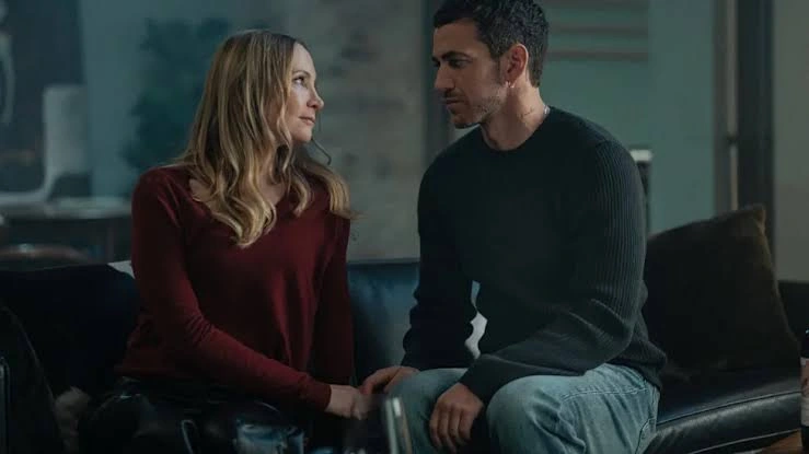 امرأة بكنزة حمراء ورجل بكنزة داكنة يجلسان متقاربين على أريكة سوداء، وتلتقي يداهما بينهما.