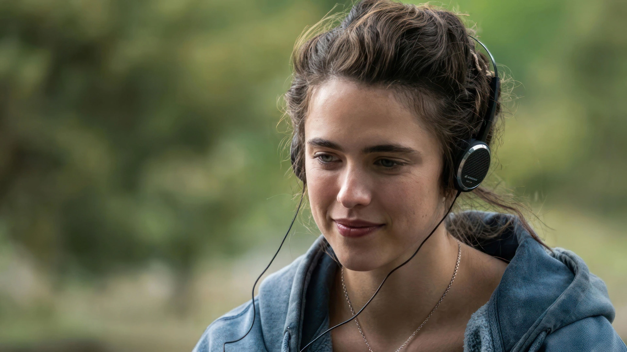 Cima wears small headphones and smiles slightly outdoors
