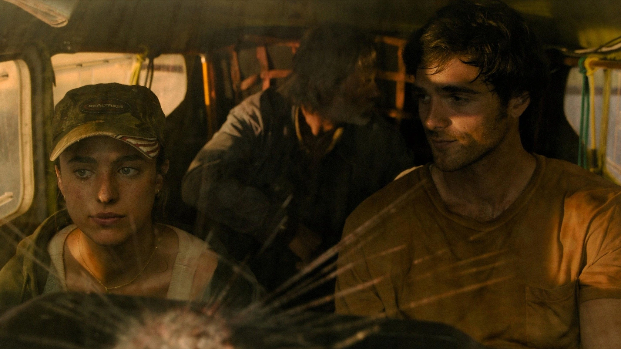 Cima and Hig sit inside a plane, with another man behind them and warm light in the cabin