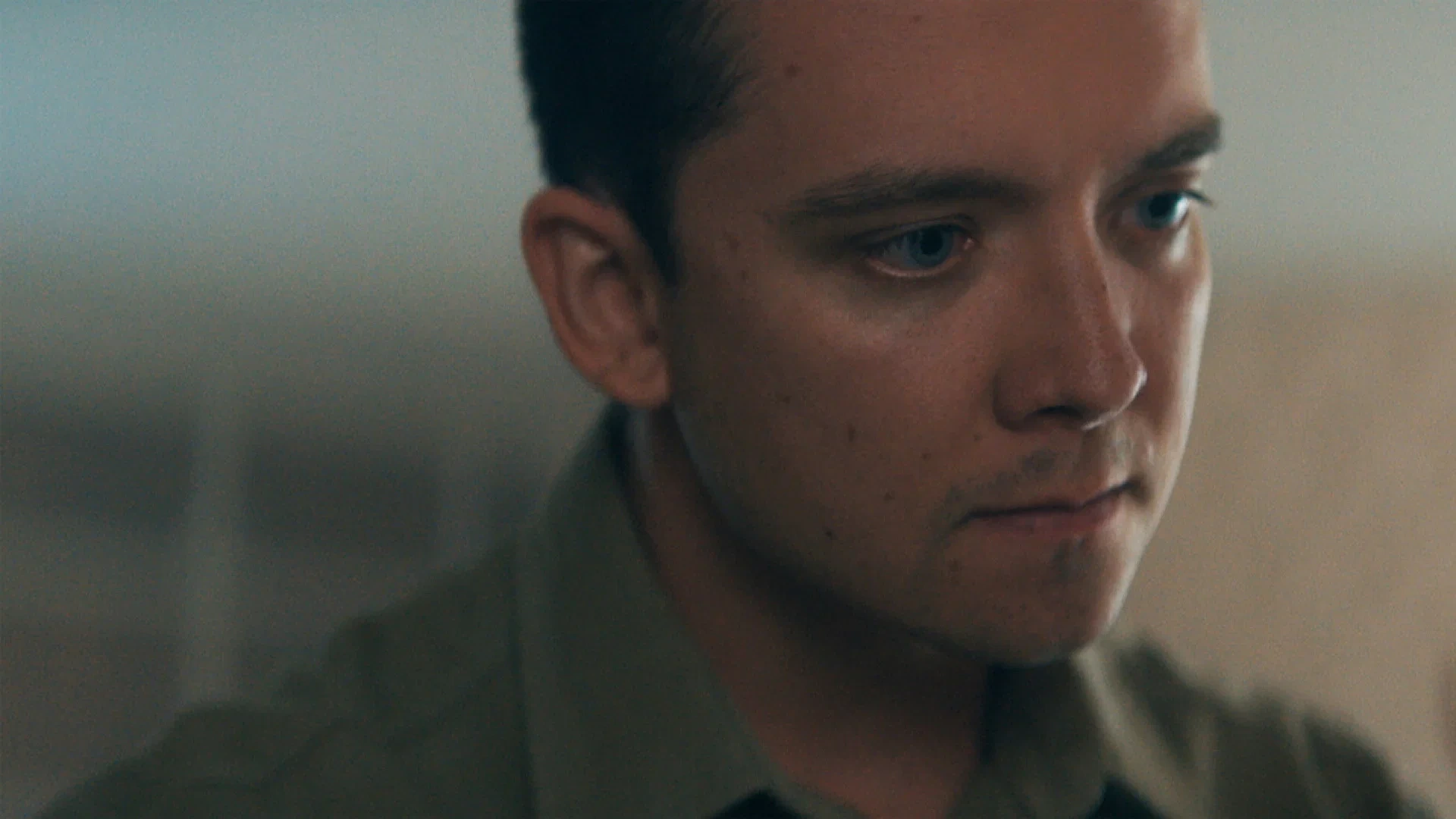A close view of a man with short hair looking to the side in a softly lit interior