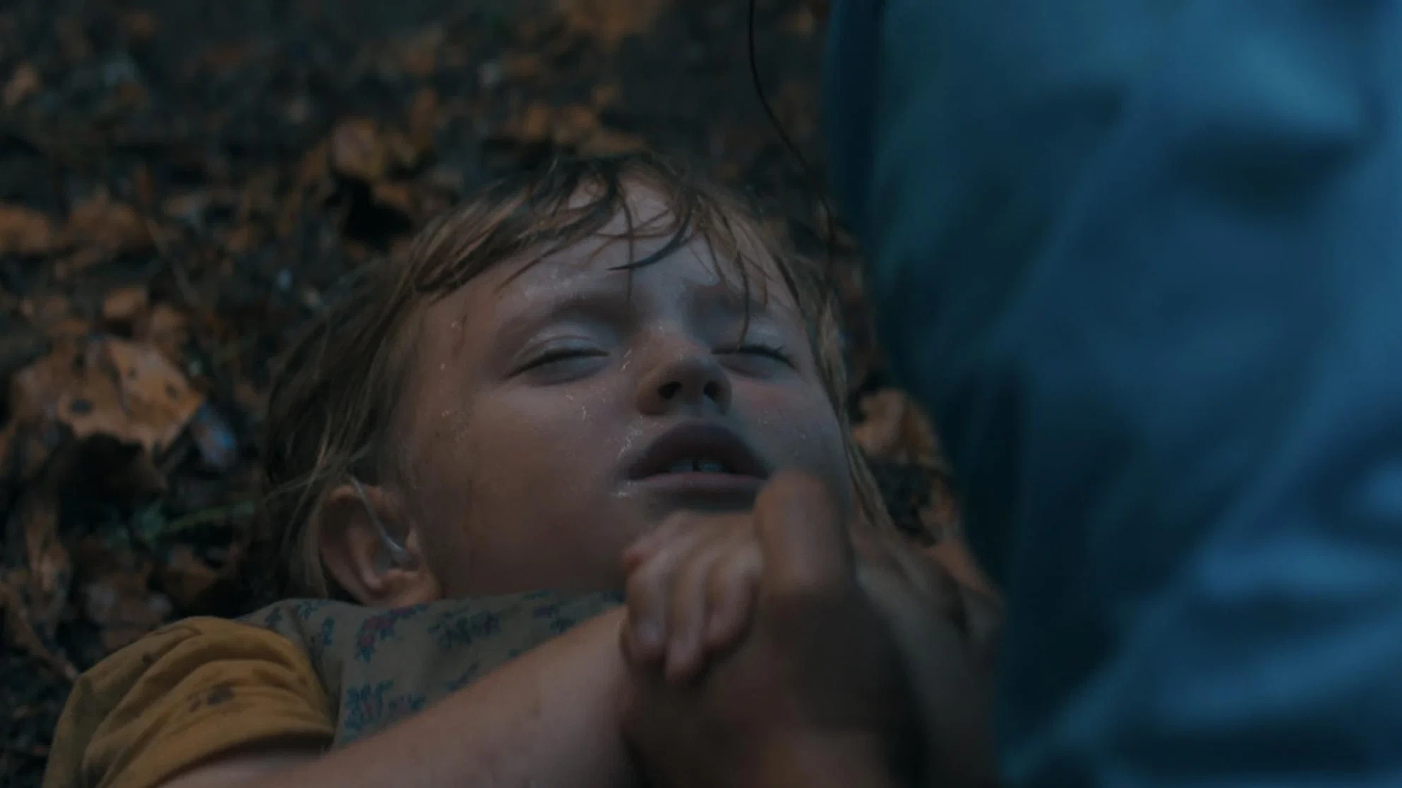 A wet child lies on the ground with her eyes partly closed and an arm in the foreground